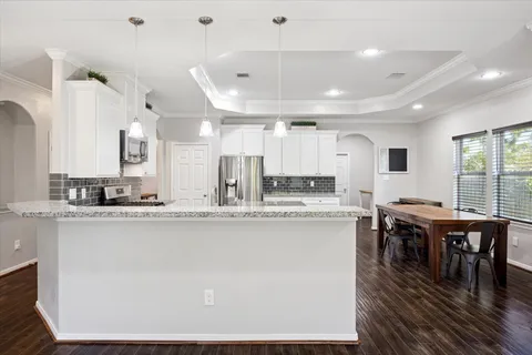 a kitchen with stainless steel appliances granite countertop a stove top oven a sink dishwasher a dining table and chairs with wooden floor