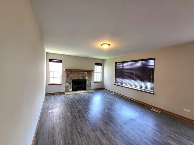 a view of an empty room with wooden floor fireplace and a window