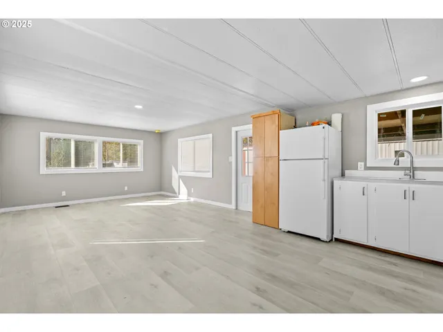 a view of an empty room with a kitchen and a refrigerator
