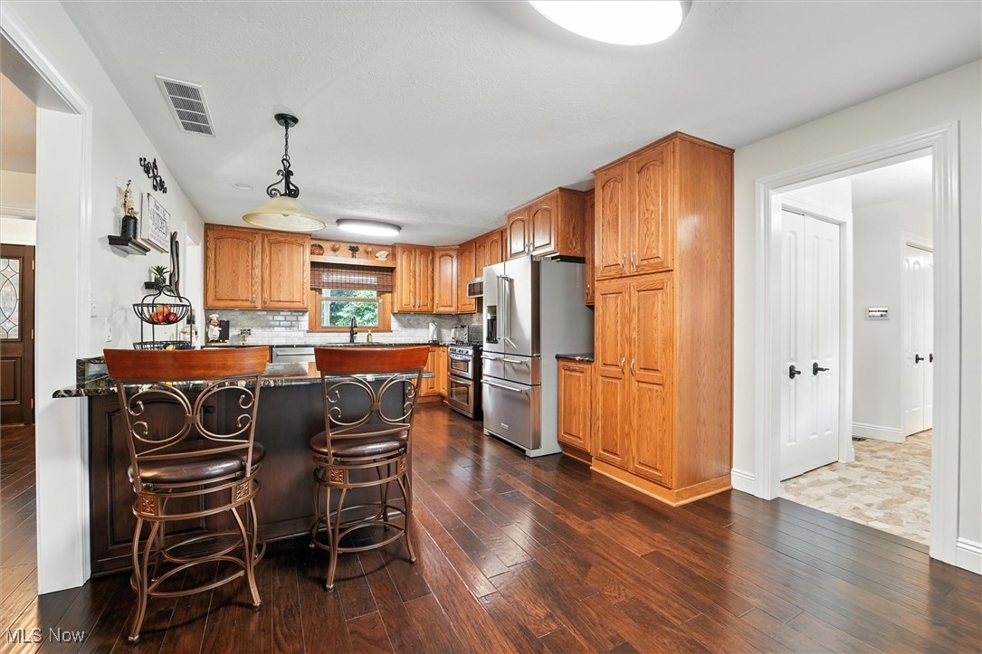 2930 South Ridge Road East Kingsville, OH 44048 - Photo 5 of 49 Kitchen with appliances with stainless steel finishes, a peninsula, decorative backsplash, dark wood-style floors, and brown cabinets