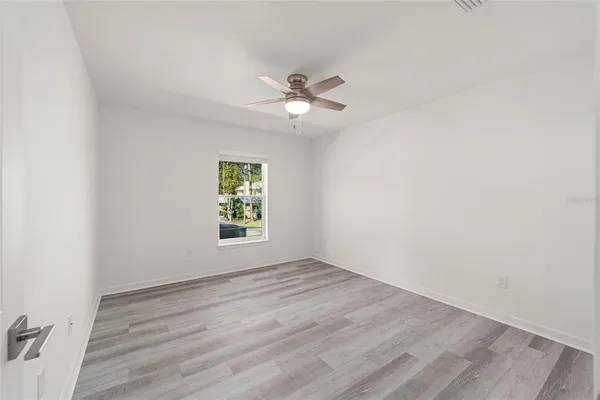 an empty room with wooden floor ceiling fan and windows