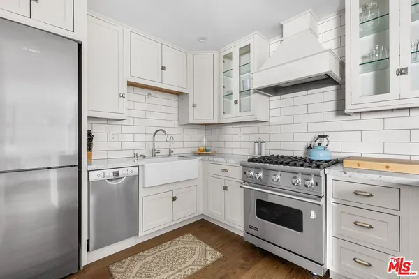 a kitchen with stainless steel appliances granite countertop a refrigerator a sink a stove and white cabinets
