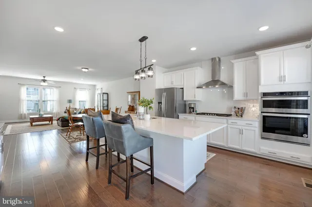 a large kitchen with kitchen island a sink stove a refrigerator and white cabinets with wooden floor