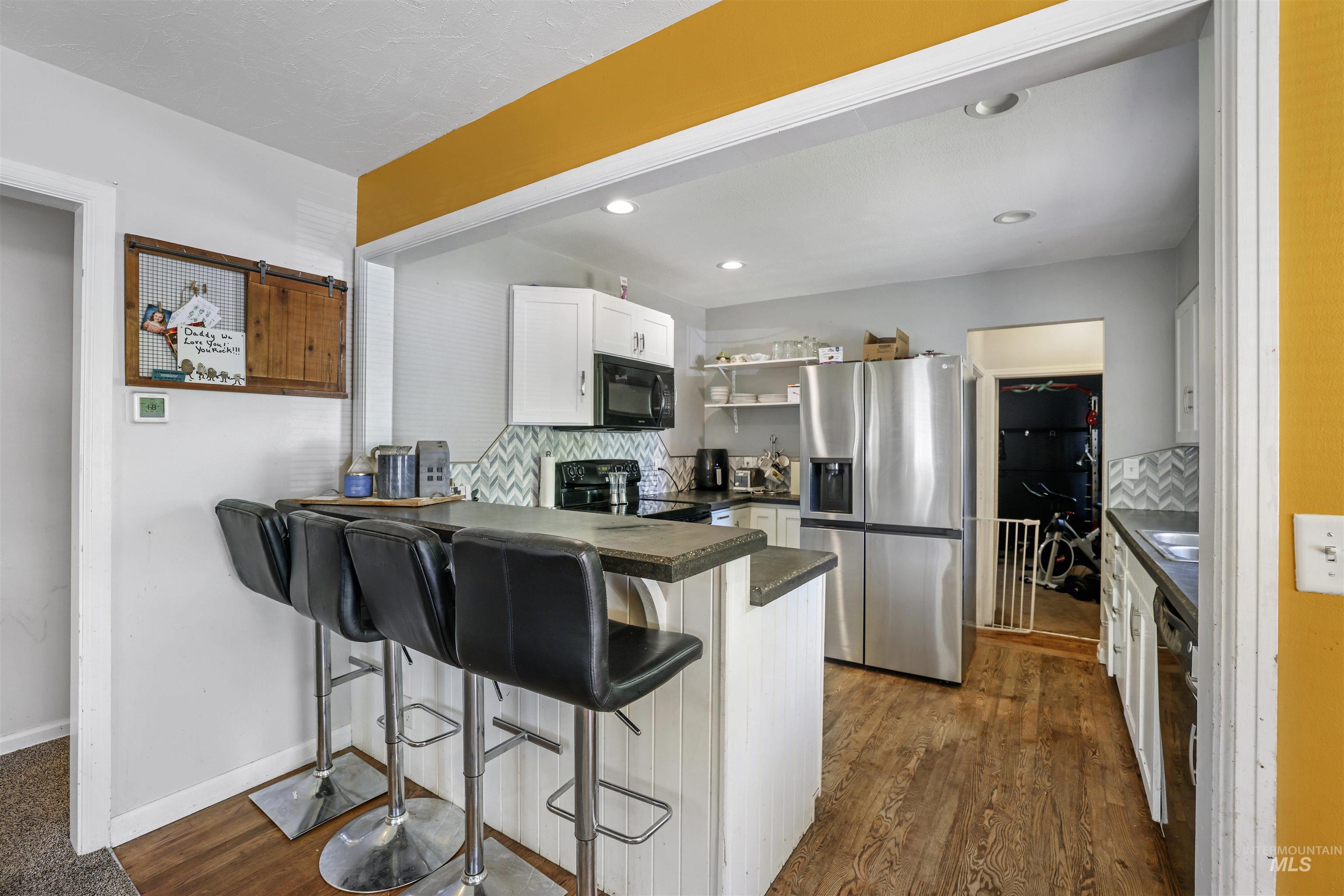 201 West 19th Street Burley, ID 83318 - Photo 7 of 31 Kitchen featuring decorative backsplash, dark countertops, white cabinets, black appliances, and a breakfast bar area