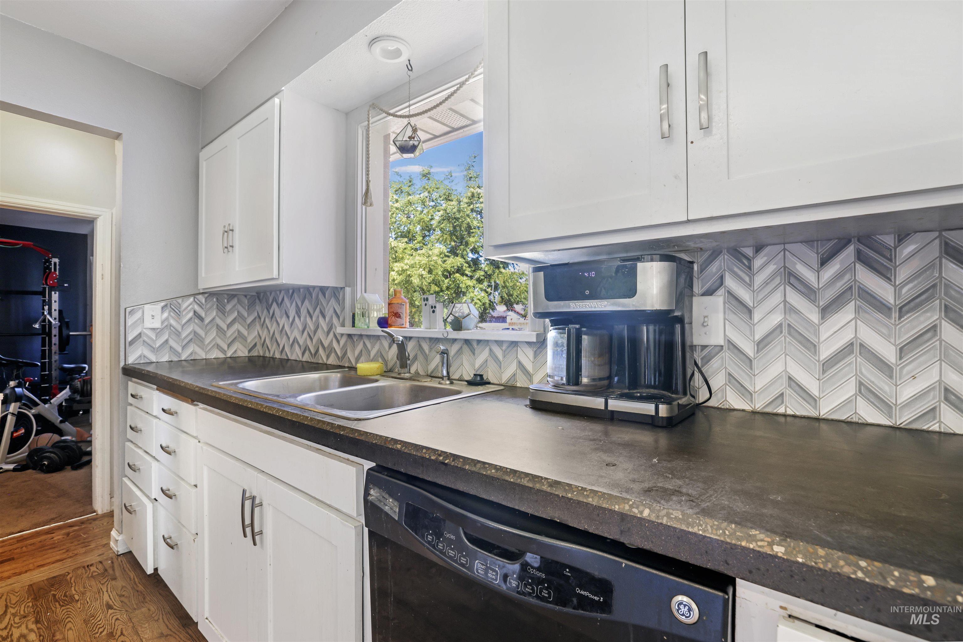 201 West 19th Street Burley, ID 83318 - Photo 10 of 31 Kitchen featuring dark countertops, decorative backsplash, black dishwasher, white cabinetry, and dark wood-type flooring