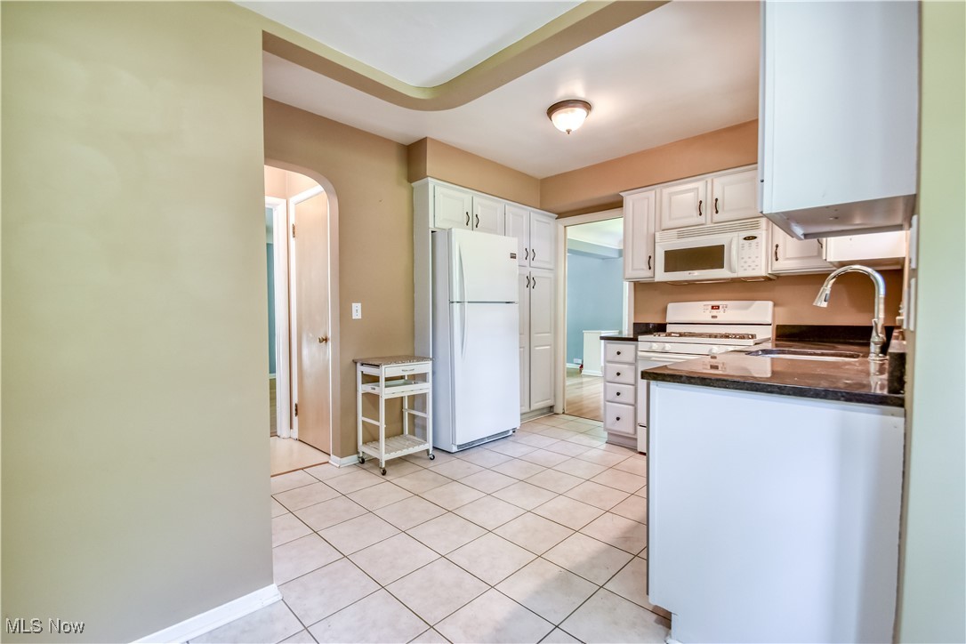 2607 Ashurst Road University Heights, OH 44118 - Photo 26 of 39 Kitchen with white appliances, arched walkways, white cabinets, light tile patterned flooring, and dark stone countertops