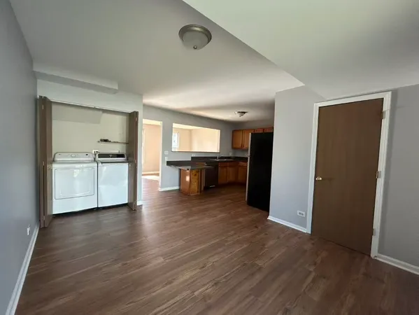 an empty room with wooden floor and a kitchen