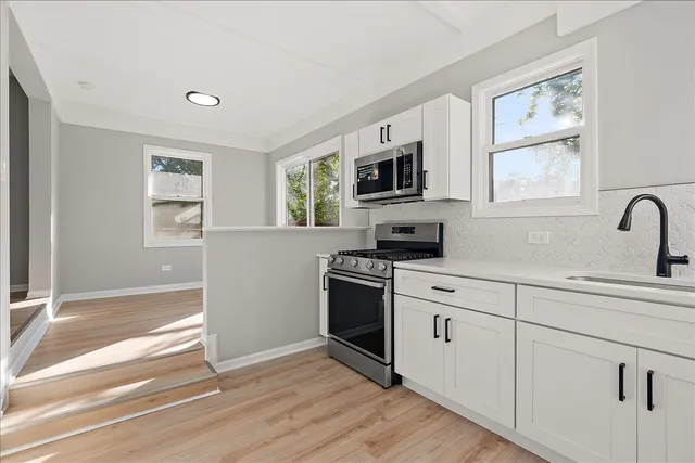 a kitchen with stainless steel appliances a white stove top oven a sink and a window with wooden floors