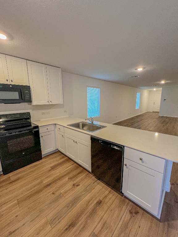 129 Hellcats Way Jarrell, TX 76537 - Photo 12 of 19 Kitchen featuring black appliances, light wood finished floors, a peninsula, light countertops, and white cabinetry