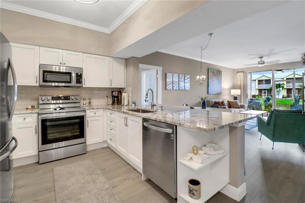 Kitchen featuring stainless steel appliances, sink, kitchen peninsula, light stone countertops, and ceiling fan with notable chandelier