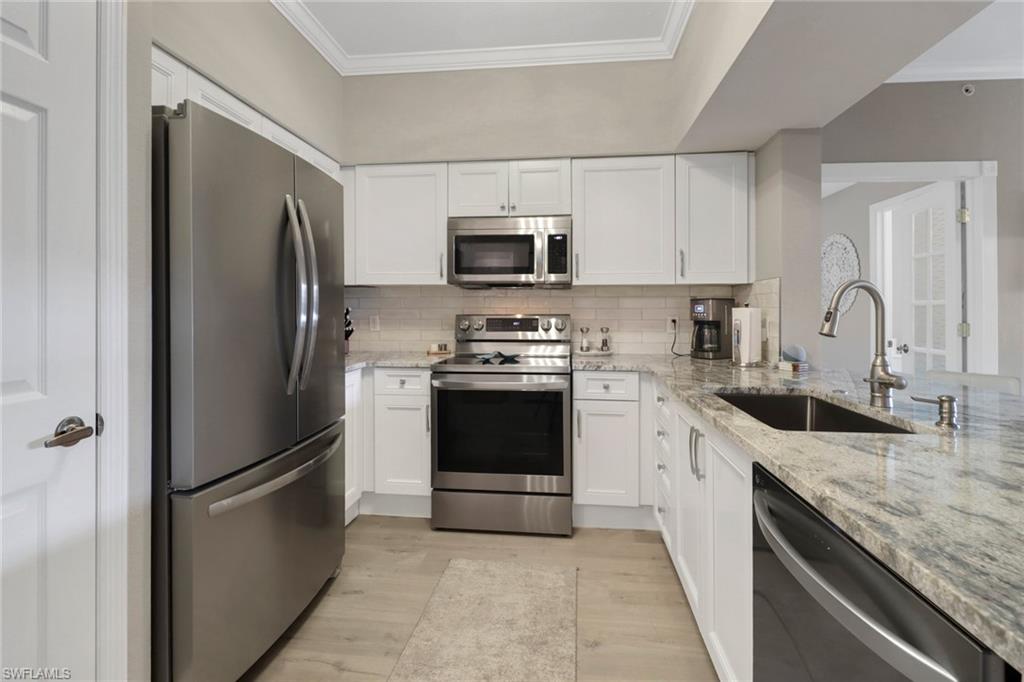 20261 Estero Gardens Circle, Unit 104 Estero, FL 33928 - Photo 5 of 50 Kitchen with stainless steel appliances, white cabinets, sink, light stone countertops, and light hardwood / wood-style floors