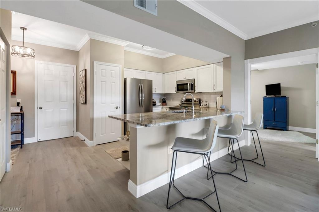 20261 Estero Gardens Circle, Unit 104 Estero, FL 33928 - Photo 6 of 50 Kitchen with appliances with stainless steel finishes, stone countertops, white cabinets, and light wood-type flooring