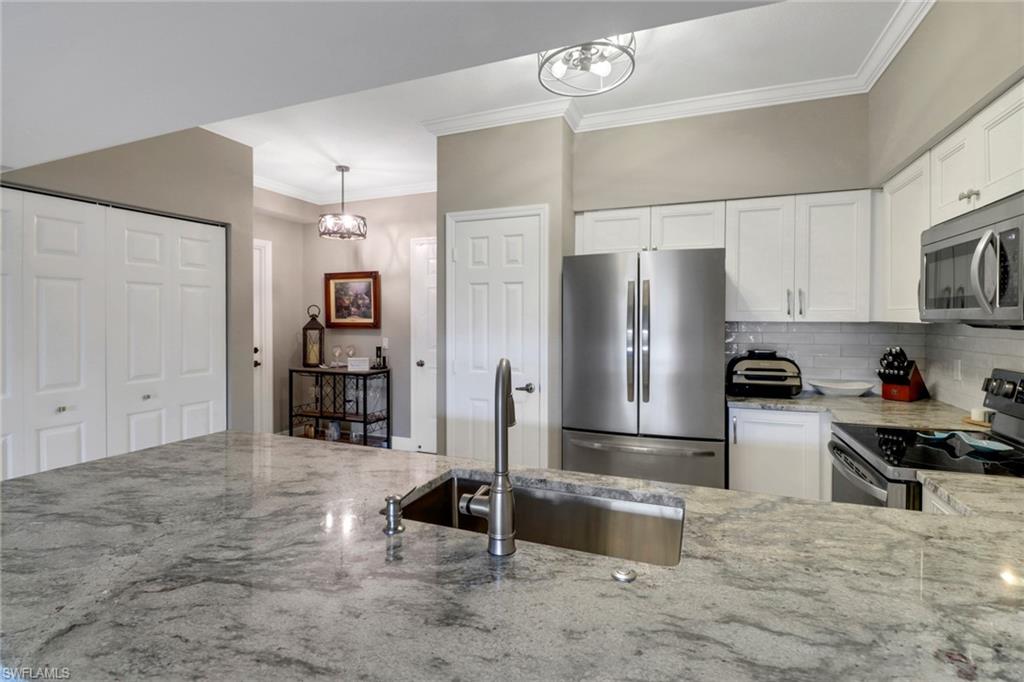 20261 Estero Gardens Circle, Unit 104 Estero, FL 33928 - Photo 7 of 50 Kitchen with white cabinetry, tasteful backsplash, light stone counters, stainless steel appliances, and sink
