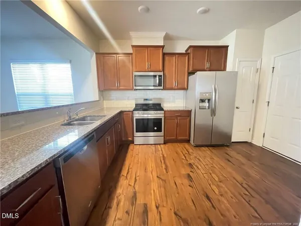 a kitchen with stainless steel appliances granite countertop a refrigerator a sink dishwasher a stove with wooden floor and cabinets