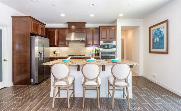 a kitchen with granite countertop a dining table chairs refrigerator and wooden floor