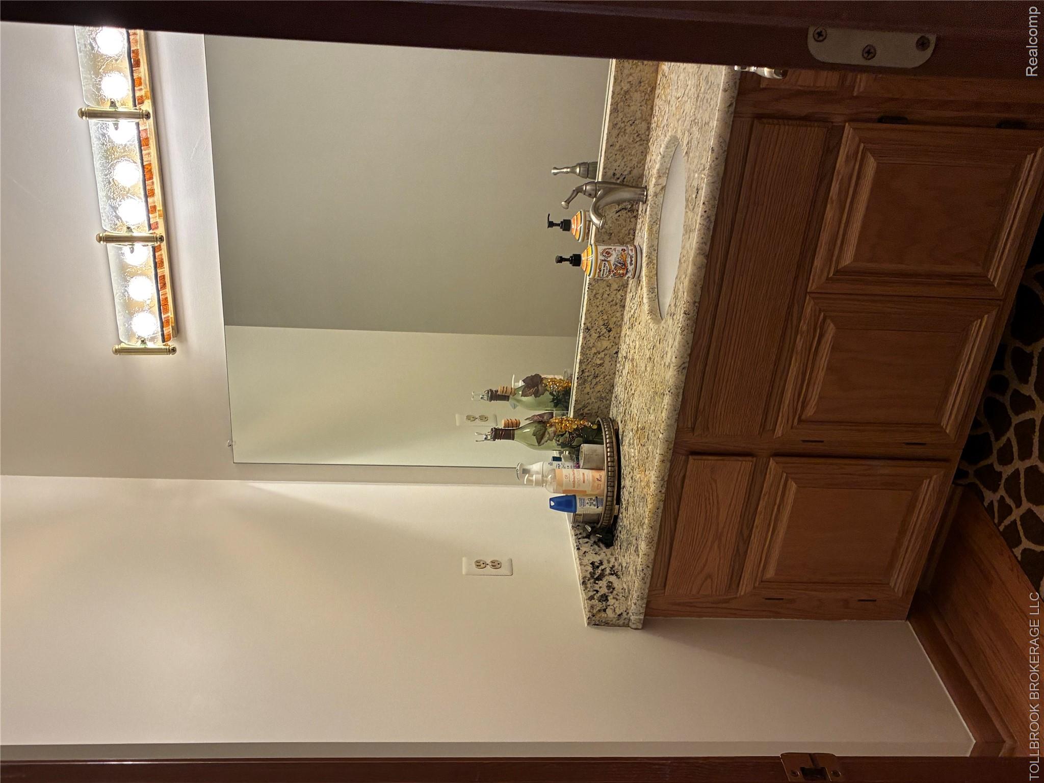 6187 Country Ridge Drive Troy, MI 48098 - Photo 15 of 23 Wood-finish flooring, wood cabinetry with paneled doors, granite-look countertop with an undermount sink, and a rectangular mirror with an overhead vanity light