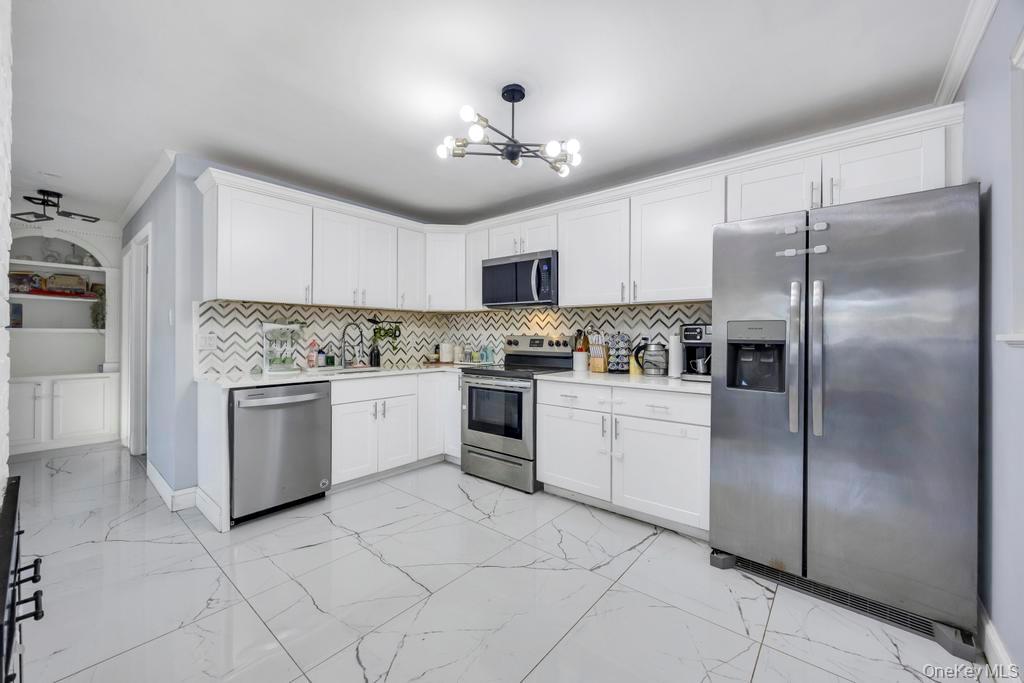 111 Blacksmith Road East Levittown, NY 11756 - Photo 6 of 14 Kitchen featuring stainless steel appliances, light marble finish flooring, white cabinets, a chandelier, and decorative backsplash