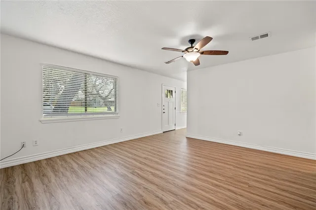 an empty room with wooden floor chandelier fan and windows
