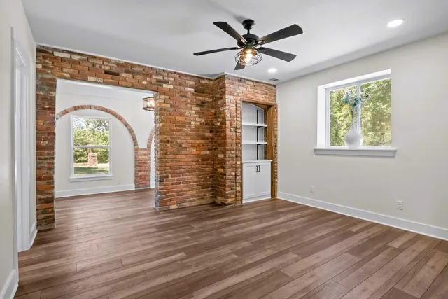 an empty room with wooden floor chandelier fan and windows