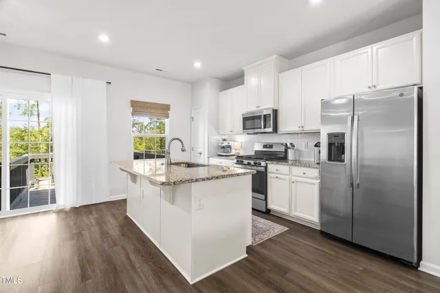 a kitchen with stainless steel appliances granite countertop a refrigerator a stove top oven a sink and dishwasher with wooden floor