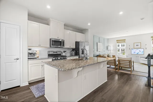 a kitchen with stainless steel appliances granite countertop a stove top oven a sink dishwasher and a refrigerator with wooden floor