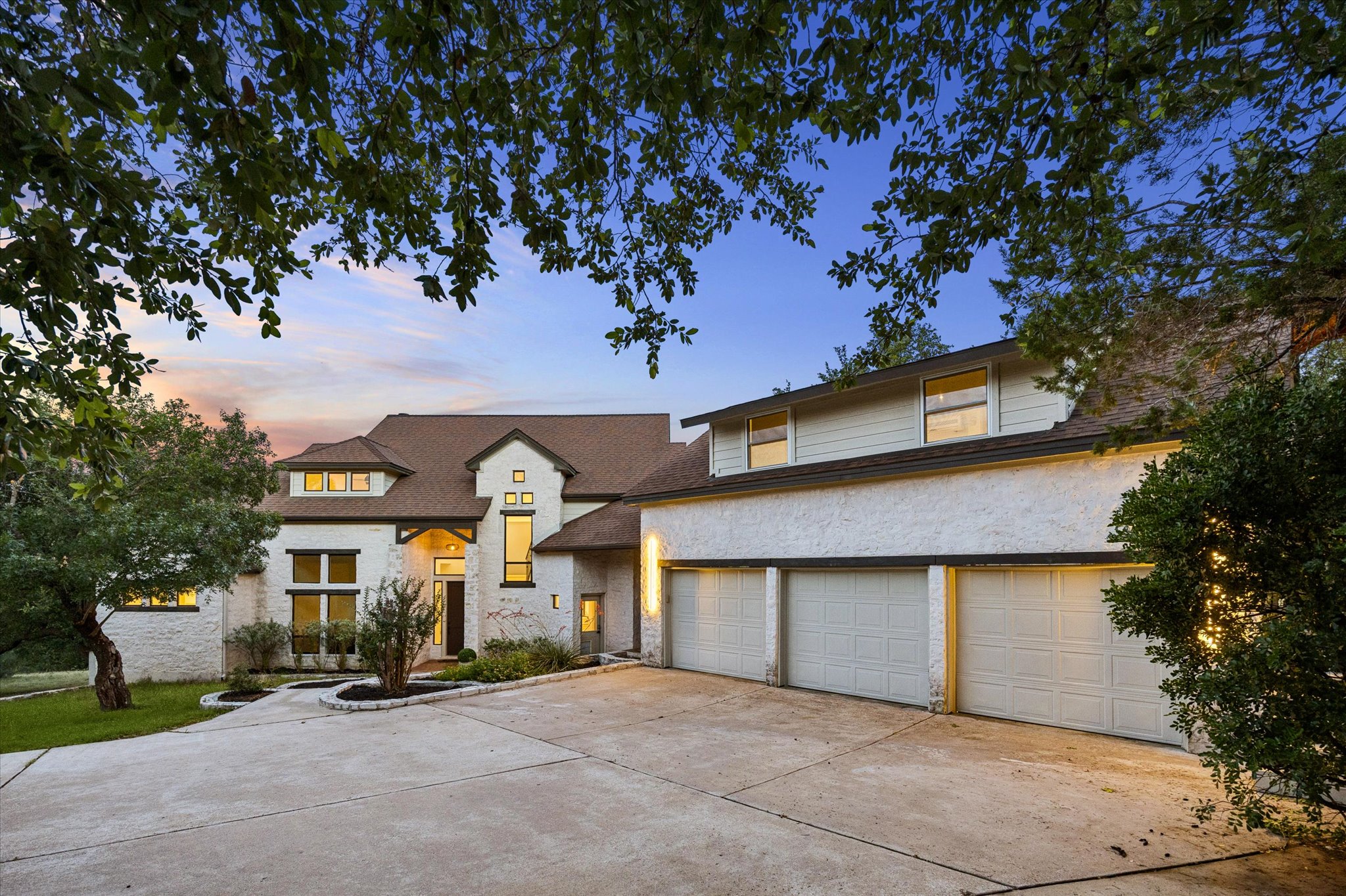 3719 Bee Creek Road Spicewood, TX 78669 - Photo 2 of 40 A spacious home with a triple garage and long concrete driveway, nestled amidst verdant landscaping.