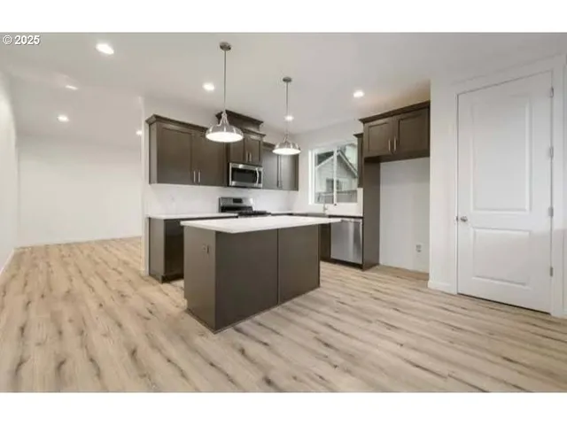 a kitchen with stainless steel appliances kitchen island a sink dishwasher a refrigerator and a oven with wooden floor