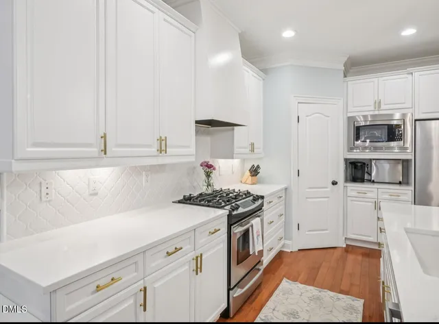 a kitchen with stainless steel appliances granite countertop a refrigerator a sink dishwasher a stove and white cabinets with wooden floor