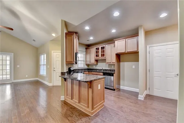 a kitchen with stainless steel appliances granite countertop a refrigerator a sink dishwasher a stove and white cabinets with wooden floor