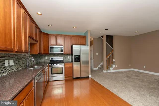 a kitchen with stainless steel appliances granite countertop a refrigerator a sink dishwasher a stove and oven with wooden cabinets