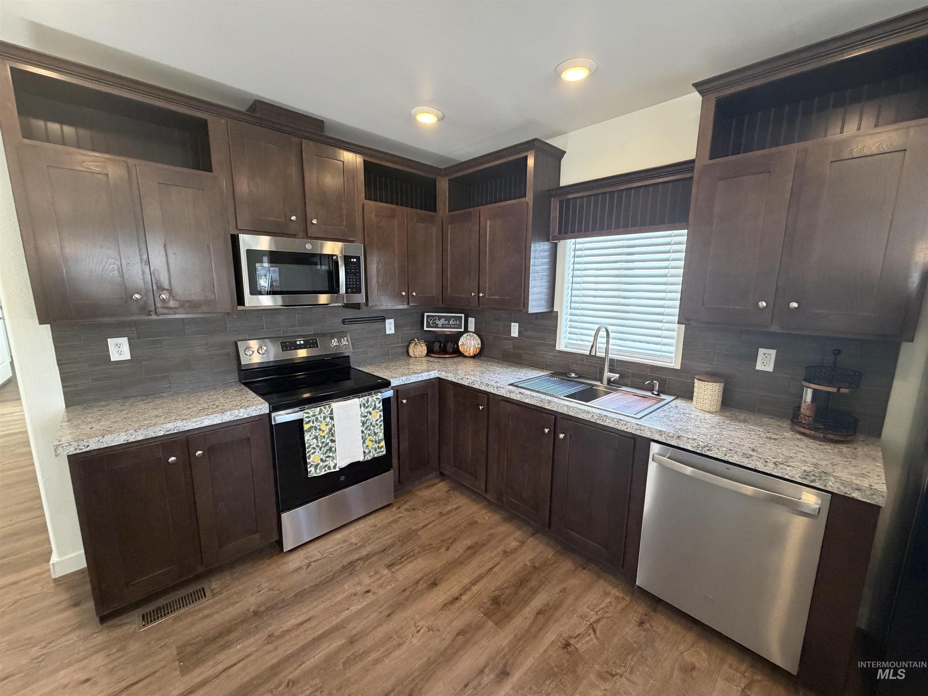 611 North Timathy Road Boise, ID 83713 - Photo 14 of 28 Kitchen featuring wood-finish flooring, dark wood cabinetry, light-colored countertops, stainless steel appliances, and a tile backsplash
