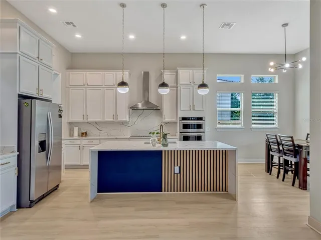 a kitchen with stainless steel appliances granite countertop a refrigerator a sink dishwasher a stove and white cabinets with wooden floor