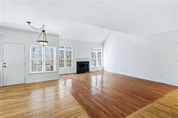 an empty room with wooden floor fireplace and windows