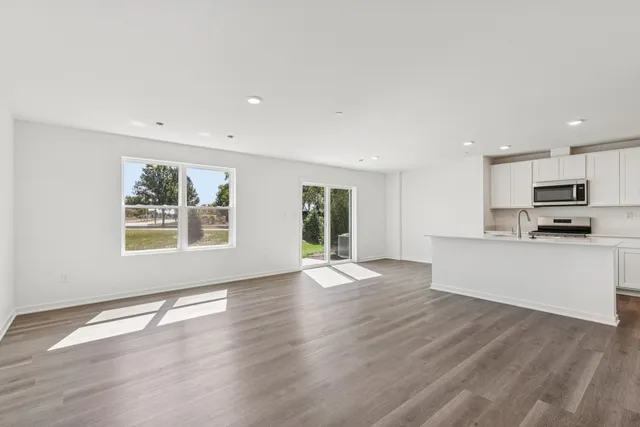a view of an empty room with kitchen and window