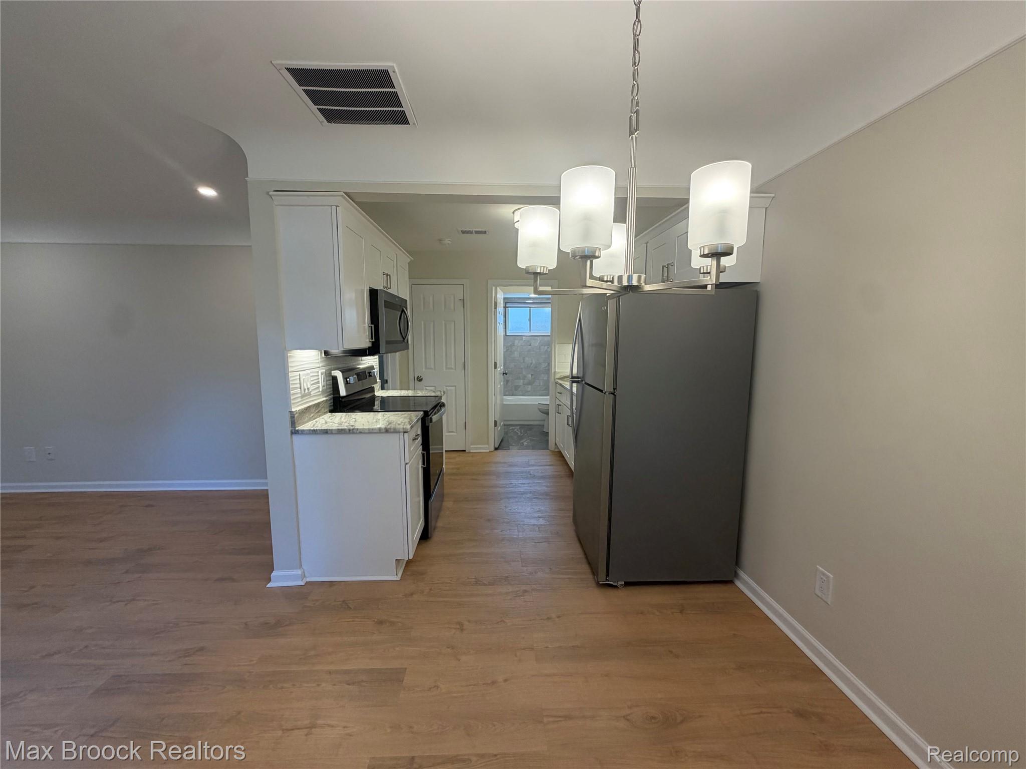 3875 Devon Road, Unit # 9 Royal Oak, MI 48073 - Photo 12 of 17 Kitchen and dining area featuring wood-finish flooring, white cabinetry, a stainless steel refrigerator, and a contemporary chandelier