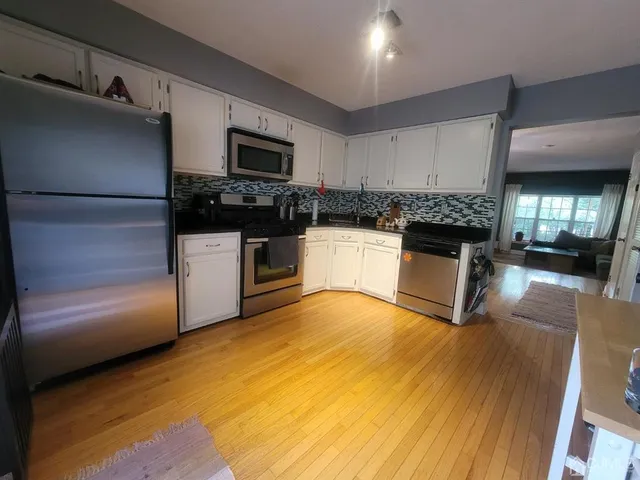 a kitchen with stainless steel appliances granite countertop a refrigerator a stove top oven a sink dishwasher and white cabinets with wooden floor