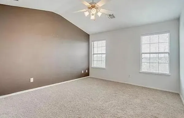 an empty room with chandelier fan and windows