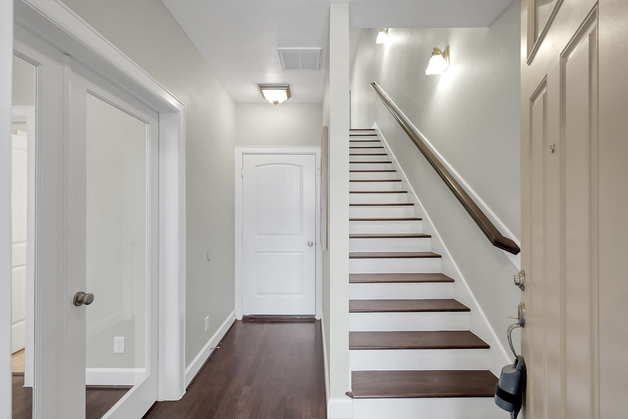 351 West 26th Street Houston, TX 77008 - Photo 23 of 45 Bright and inviting entryway featuring a staircase with dark wooden steps and white risers. The space is well-lit with modern wall sconces, and there are doors leading to additional rooms.