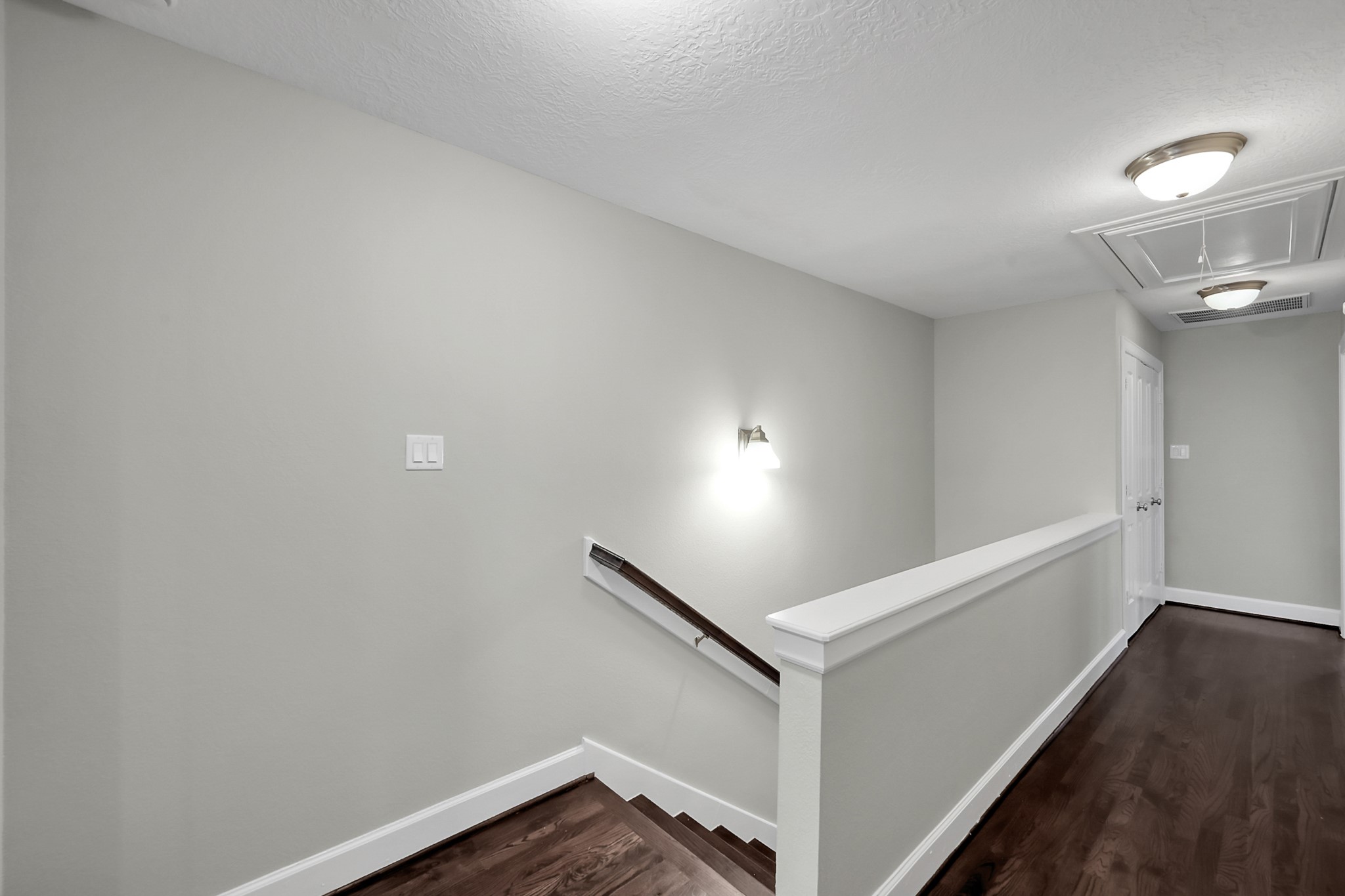 351 West 26th Street Houston, TX 77008 - Photo 24 of 45 This photo shows a modern, well-lit stairway with hardwood flooring and white walls. The hallway features recessed lighting and a simple handrail, leading to a door at the end.