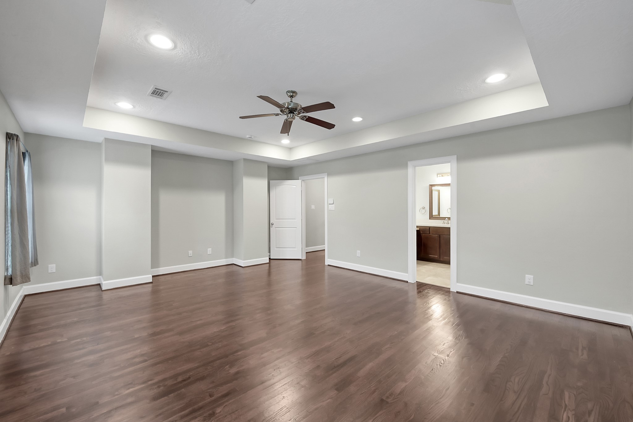 351 West 26th Street Houston, TX 77008 - Photo 26 of 45 This ample room features elegant wood flooring, a tray ceiling with recessed lighting, and a ceiling fan. It leads into an en-suite bathroom, offering convenience and comfort. Perfect for a master bedroom or versatile living space.