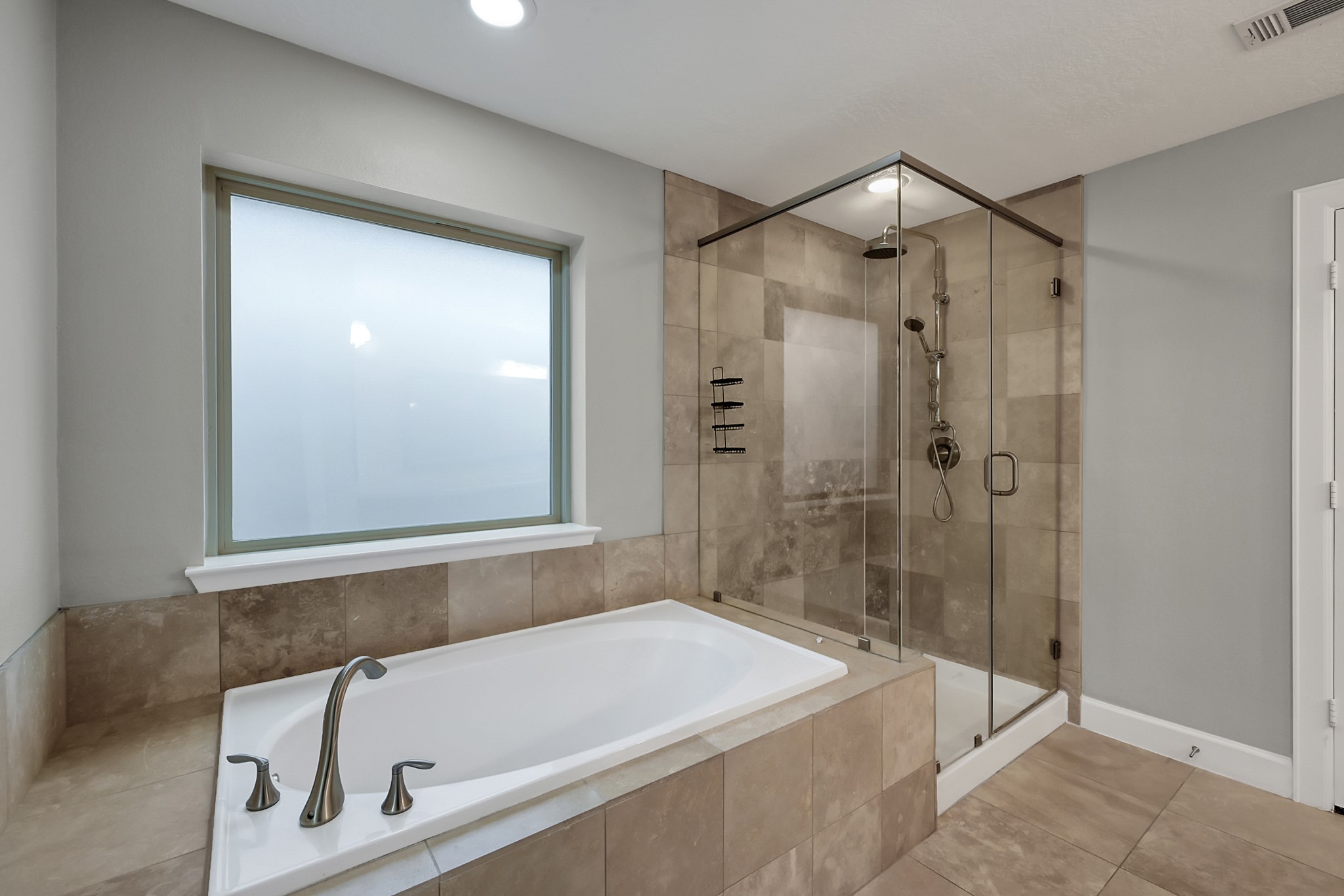351 West 26th Street Houston, TX 77008 - Photo 28 of 45 This modern bathroom features a spacious bathtub with sleek fixtures and a glass-enclosed shower. The neutral tile design and frosted window provide a clean and elegant look.
