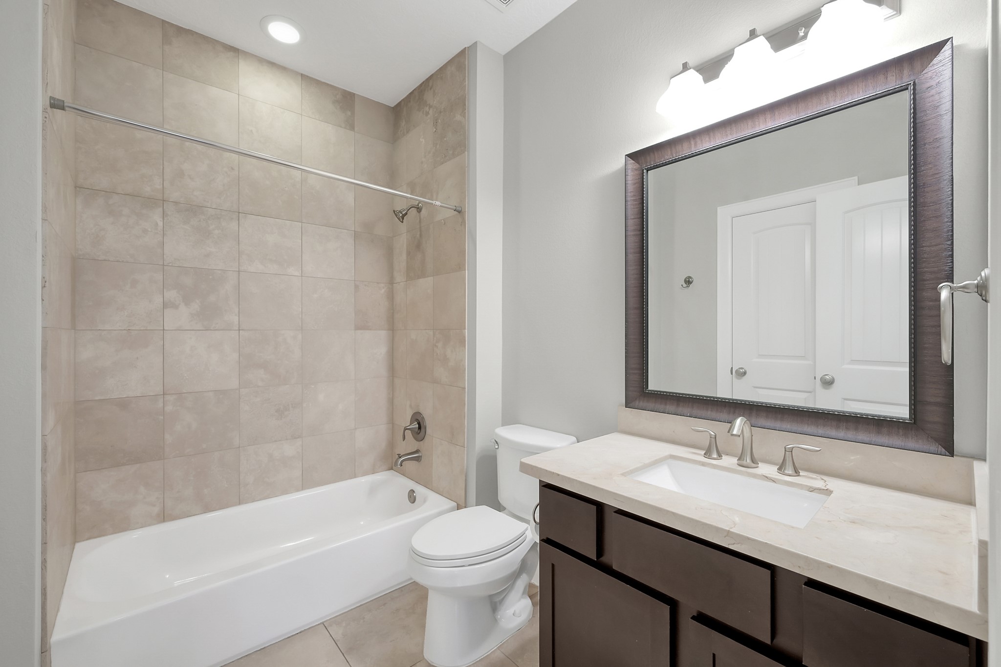 351 West 26th Street Houston, TX 77008 - Photo 35 of 45 This bathroom features a clean, modern design with beige tile surrounding the bathtub and shower area. It includes a sleek vanity with a large mirror, under-cabinet storage, and contemporary fixtures. The neutral color palette enhances its spacious and inviting feel.