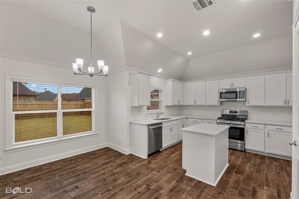 304 Prien Lk Loop Bossier City, LA 71111 - Photo 15 of 39 Vaulted ceiling kitchen featuring white cabinetry, stainless steel appliances, a central island with a solid surface countertop, and wood-finish flooring