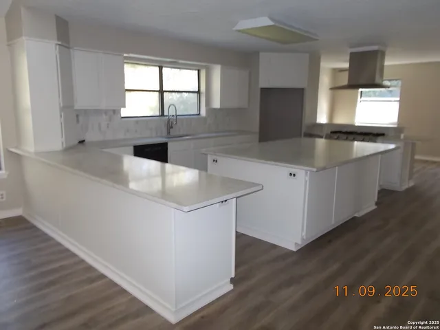 a kitchen with granite countertop a stove a sink and white cabinets with wooden floor
