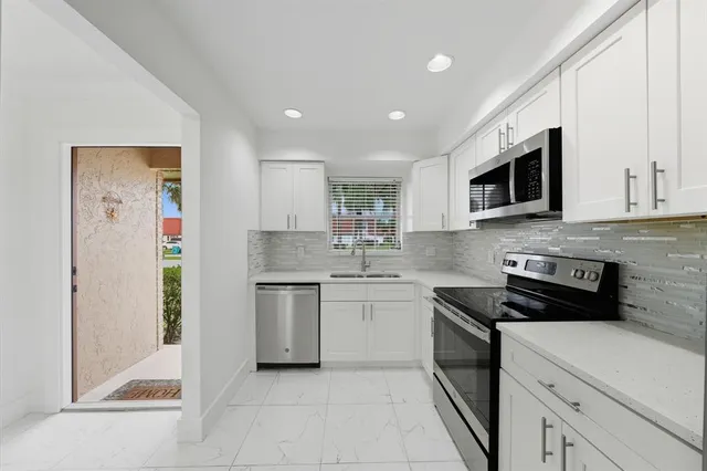 a kitchen with granite countertop white cabinets appliances and a window