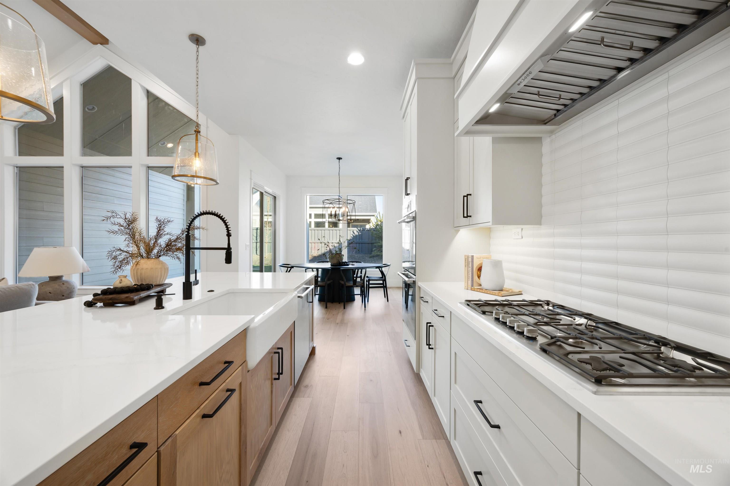 1034 East Escalation Street Meridian, ID 83642 - Photo 12 of 40 Kitchen with white cabinetry, custom exhaust hood, hanging light fixtures, appliances with stainless steel finishes, and light wood-style flooring