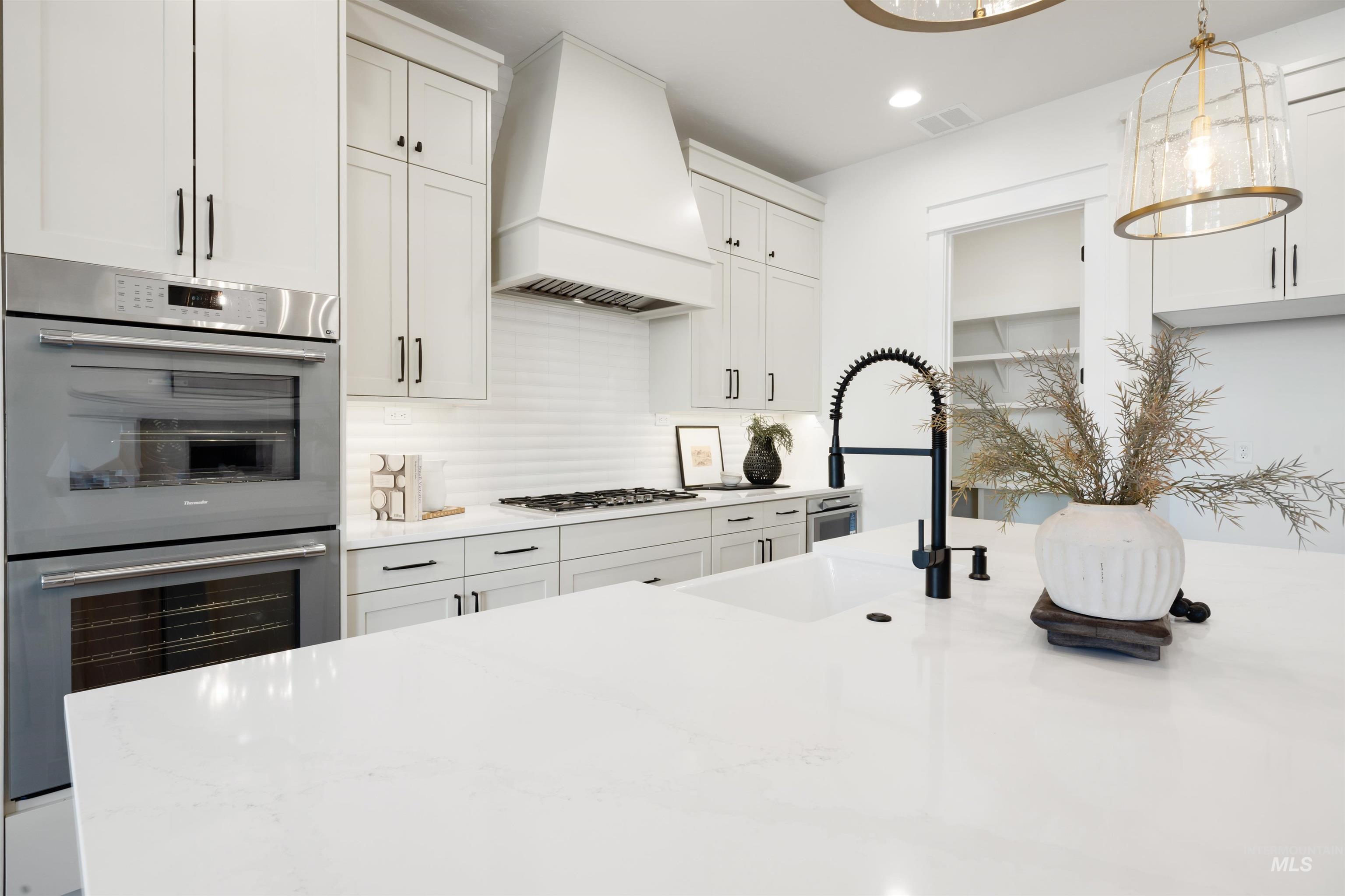 1034 East Escalation Street Meridian, ID 83642 - Photo 15 of 40 Kitchen featuring stainless steel appliances, white cabinetry, premium range hood, light stone countertops, and recessed lighting