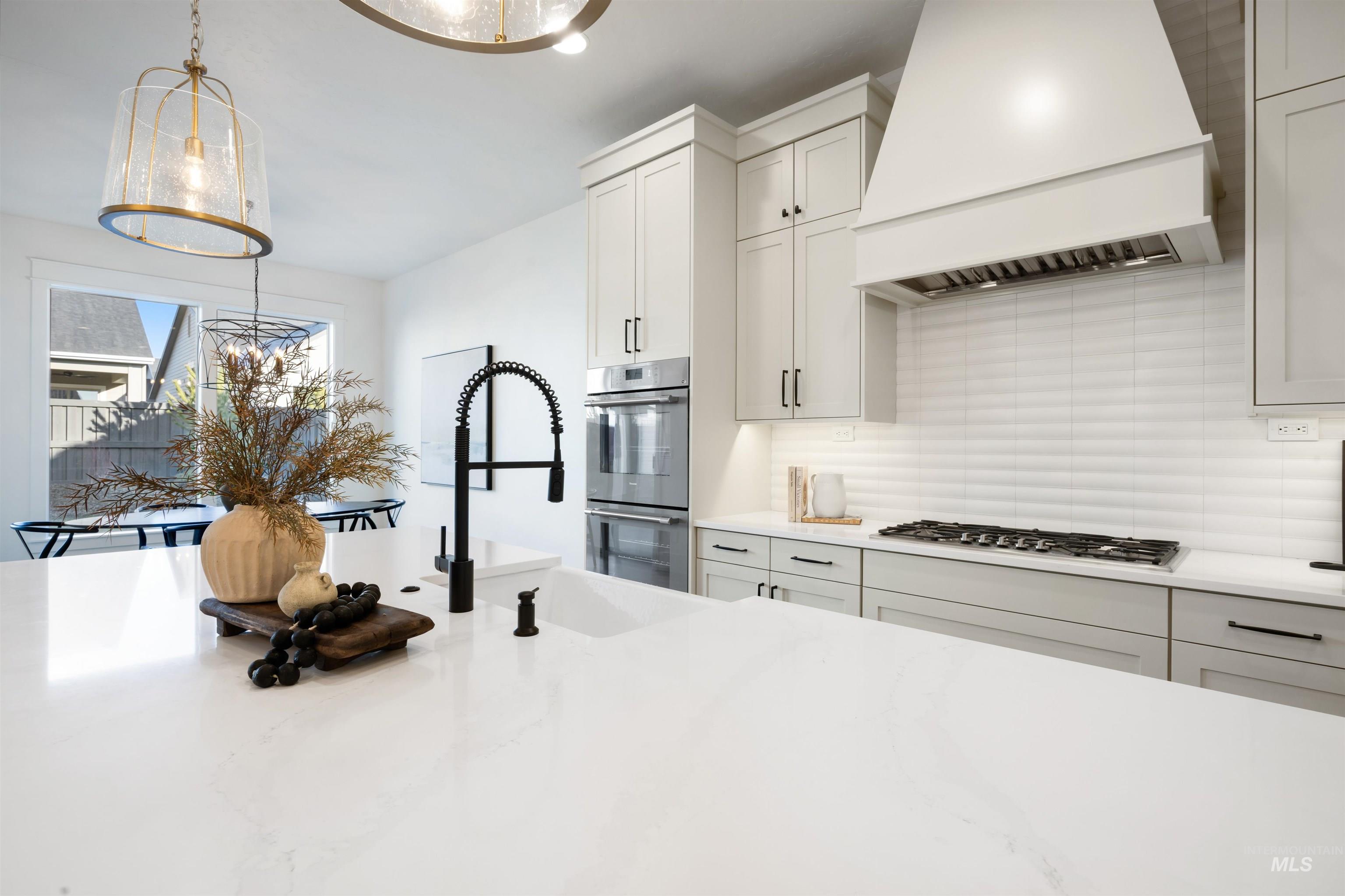 1034 East Escalation Street Meridian, ID 83642 - Photo 16 of 40 Kitchen with custom range hood, pendant lighting, appliances with stainless steel finishes, white cabinetry, and light stone counters