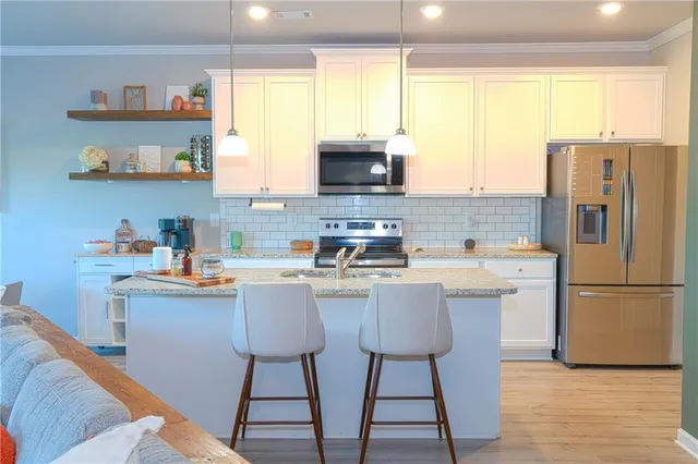 a kitchen with stainless steel appliances kitchen island granite countertop a refrigerator a sink a stove and white cabinets with wooden floor