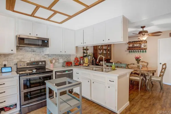 a kitchen with stainless steel appliances a stove a sink a dining table and chairs with white cabinets